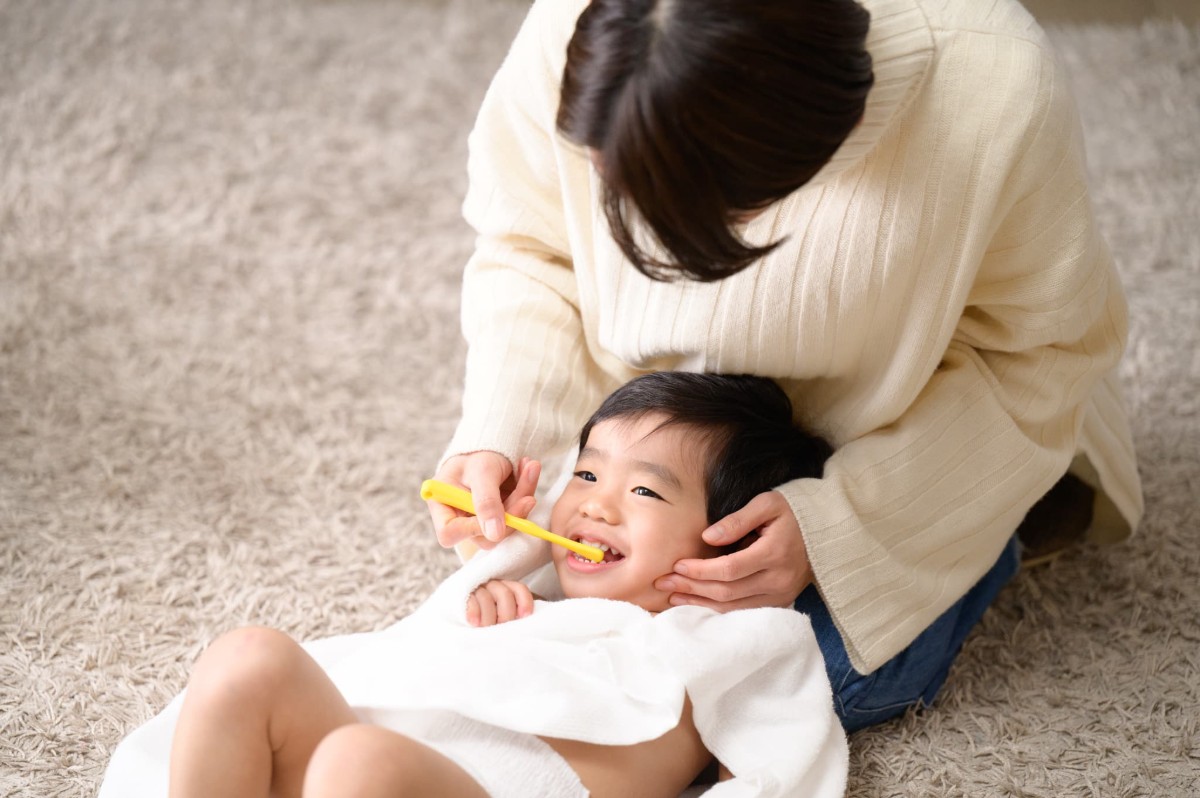 母親に仕上げ磨きをしてもらう子ども