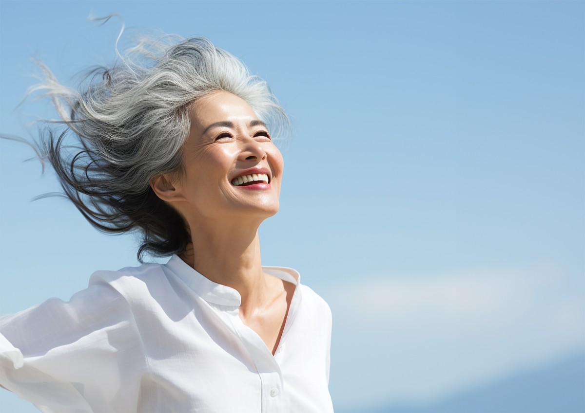 青空の下で風を受けて立っている笑顔の女性